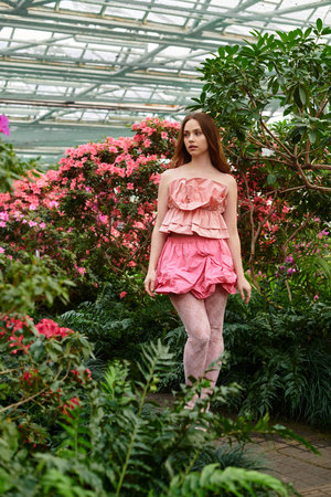 A lovely young woman enjoys nature among colorful flowers in a vibrant greenhouse.の写真素材