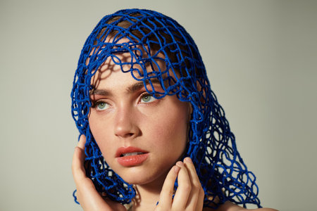 A young beautiful woman showcases her captivating features while gently holding her face.