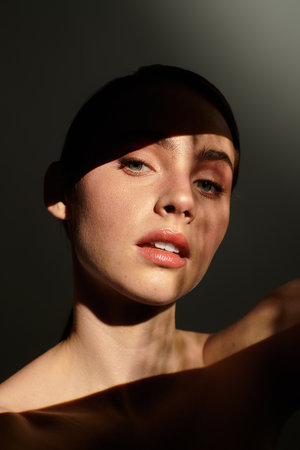 Young woman showcases natural beauty with playful shadows on her radiant skin, evoking artistry.の写真素材
