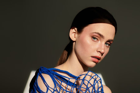 A striking young woman in a blue outfit is highlighted by soft lighting.の写真素材