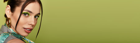 A beautiful young woman with bold eye makeup poses confidently against a green backdrop.の写真素材