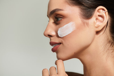 A young woman applies a creamy product to her skin, reflecting on her skincare journey.