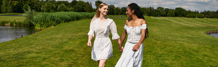 Two women walk hand in hand, smiling joyfully as they embrace love and connection outdoors.の写真素材