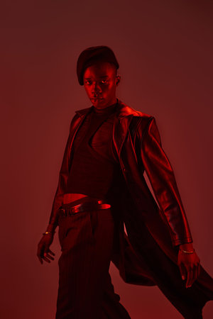Stylish young man showcases confidence and flair in a red lit backdrop, embodying modern fashion.