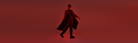 A stylish young man strides confidently in a captivating red lit ambiance, radiating charm.