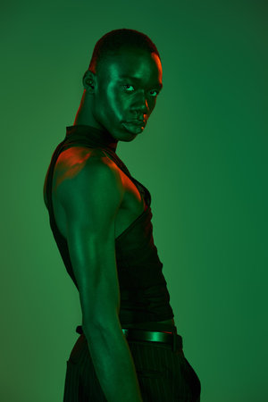 A confident young man dressed in fashionable attire stands against a striking green backdrop.の写真素材