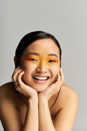 A young Asian woman smiles, displaying vibrant eye makeup against a neutral background.の写真素材