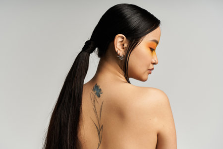 A young Asian woman turns gracefully, showcasing her floral tattoo with confidence.の写真素材
