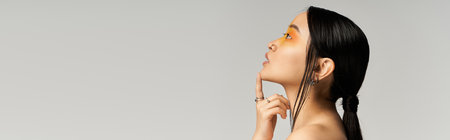A young Asian woman poses gracefully, fingers on her chin, highlighting artistic makeup.の写真素材