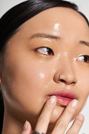 Young beautiful woman gently touching her face, glowing skin illuminated by warm sunset light.の写真素材