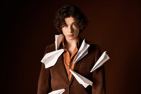 A young man with curly hair confidently wears a brown corduroy blazer with paper planes.の写真素材