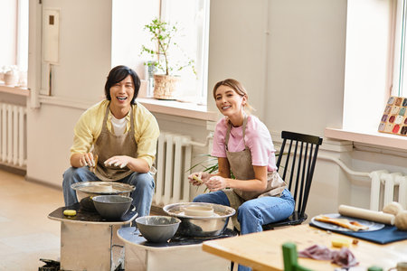 A young couple enjoys a fun and playful pottery session, laughing and creating together.のeditorial素材