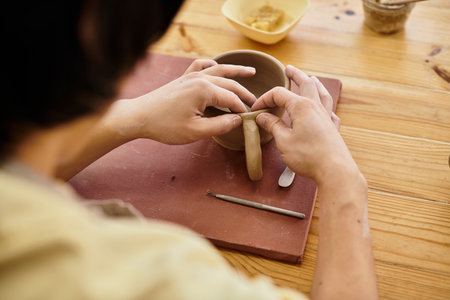 Hands skillfully shape clay into a distinctive mug within a well lit pottery studio.の写真素材