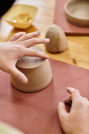 Hands skillfully shape unglazed clay into beautiful pottery in a bright studio environment.