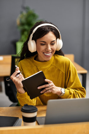 In a lively office, a young woman in headphones happily takes notes as she focuses.