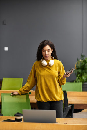 Beautiful woman in a bright sweater stands in a contemporary office, focusing on her work tasks.のeditorial素材