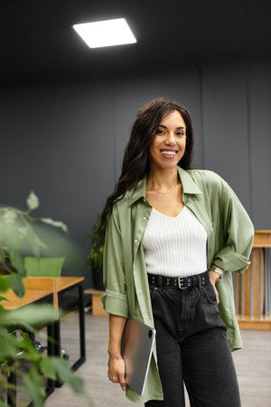 Young and beautiful woman stands in a stylish office, showcasing elegance while working.