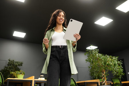 A confident young woman uses a tablet in a modern office adorned with plants.