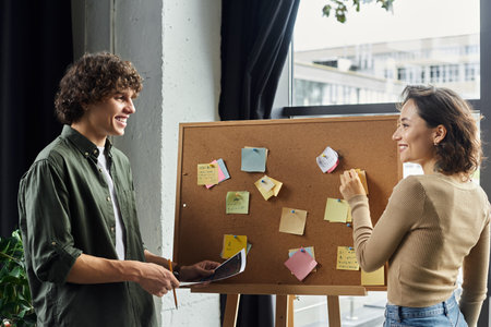 Two coworkers happily share ideas around a corkboard filled with colorful notes.