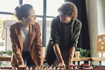 Colleagues share laughter and strategy while enjoying a foosball game in a modern workspace.の写真素材