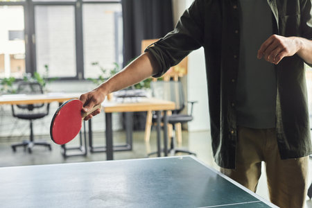 A person skillfully readies to hit a ping pong ball in a modern office with workstations.の写真素材