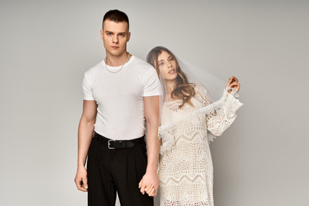 Young couple holds hands in elegant attire, radiating love and a dreamy vibe.