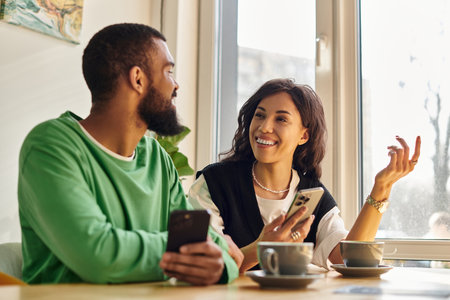 Two smiling individuals enjoy a pleasant conversation over coffee in a warm cafe ambiance.のeditorial素材