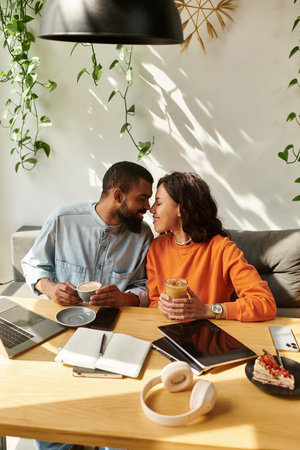 Couple working on laptops while sharing drinks and a dessert in a comfortable cafe setting.の写真素材
