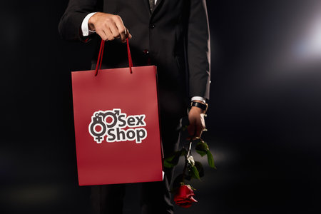 A young and handsome man stands confidently, clutching a red bag and a rose in dim lighting.の写真素材