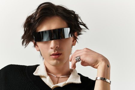 A handsome young man in an edgy outfit poses confidently in a contemporary studio space.