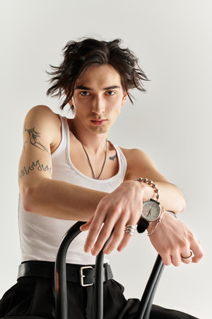 A stylish young man leans on a chair in a minimalistic studio, highlighting his look.