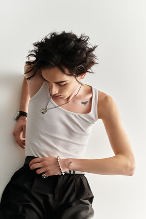 A slim young man in a white tank top poses confidently against a plain backdrop.
