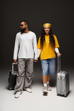A fashionable couple holds hands while standing with their suitcases, ready for travel.