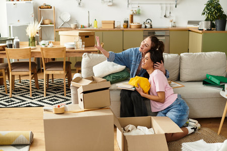 Two women embrace happily as they unpack in their cozy living space, surrounded by boxes.