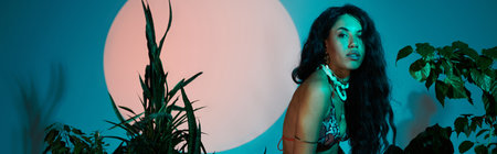 A young woman poses gracefully among vibrant plants, highlighting her fashion style.のeditorial素材