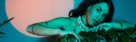 A stunning young woman showcases her summer fashion amidst lush greenery under vibrant lighting.
