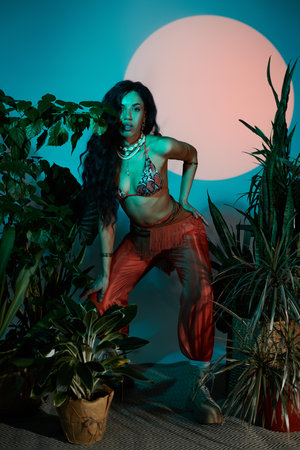 A young woman stands boldly among lush greenery, exuding confidence in summer fashion.