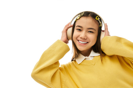 A happy Asian schoolgirl in a stylish uniform poses in a bright studio, enjoying music.