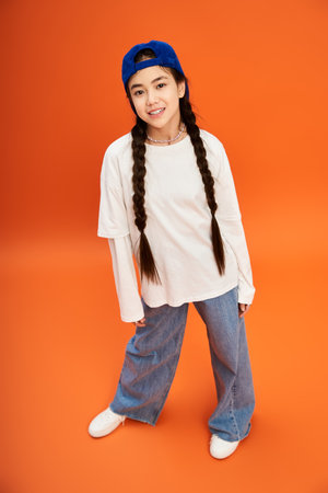 A trendy teenage girl showcases her fashion sense with confidence against an orange backdrop.のeditorial素材