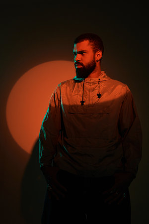 A young man stands confidently in artistic lighting, showcasing summer vibes and modern fashion.