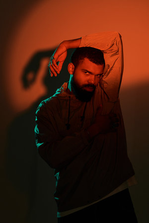 A handsome man showcases a striking look with bright lighting while posing confidently indoors.