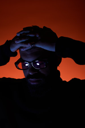 A young man with stylish glasses poses with a contemplative expression, surrounded by warm hues.