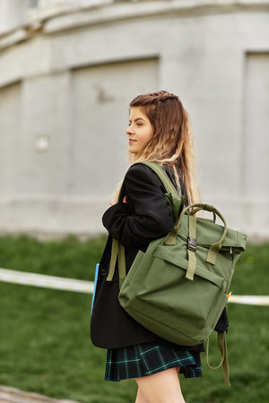 A young woman in a fashionable uniform strolls confidently on a vibrant college campus.