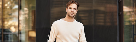 A handsome man strolls with confidence amidst modern architecture during the afternoon.