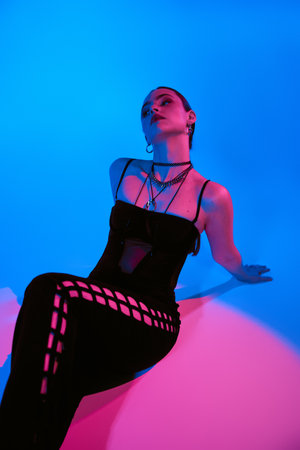 A beautiful young woman poses gracefully in a chic outfit, illuminated by pink and blue lights.