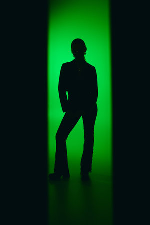 A young woman in a sleek black outfit poses gracefully, surrounded by vibrant green light.の写真素材