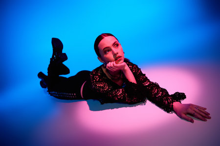 A young woman in a trendy outfit lounges gracefully under striking pink and blue lights.