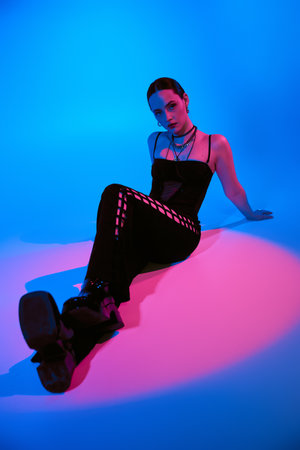 Stylish young woman poses confidently in a chic outfit, illuminated by colorful lighting.