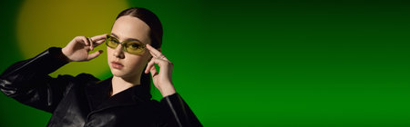 A stylish young woman models a chic black outfit against a vibrant green backdrop, banner