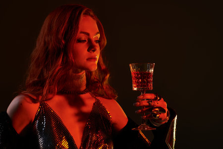 A beautiful young woman, elegantly dressed, holds a sparkling glass in a dimly lit atmosphere.